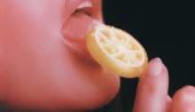 A woman taking a bite out of a lemon